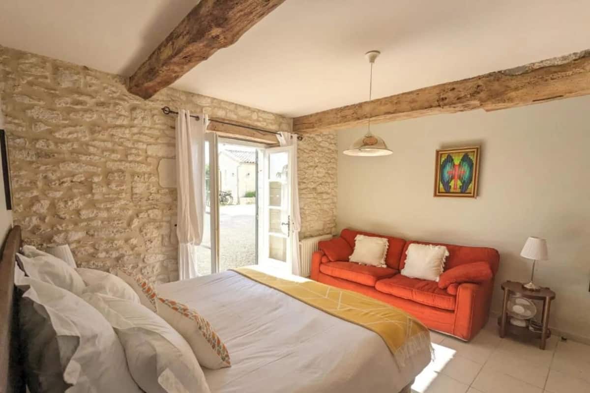 Una camera da letto con parete in pietra, un letto con biancheria bianca, un divano rosso e un quadro appeso al muro.