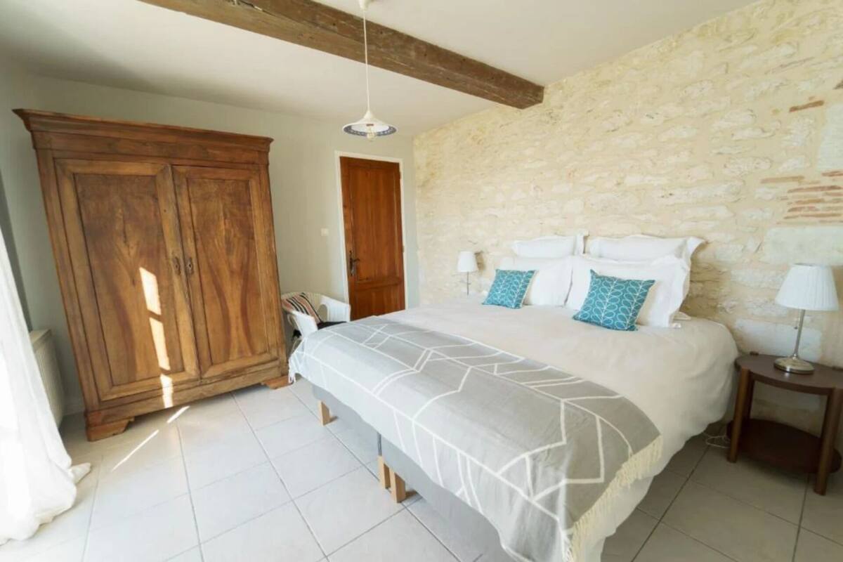 Una camera da letto con un letto, un armadio in legno, un muro in pietra e un comodino con una lampada.