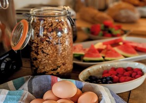 Ein Frühstückstisch mit einem Granola-Glas, einer Schale mit Beeren, einem Teller mit Wassermelone und einer Serviete mit Eiern.