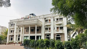 A multi-story building with a classical architectural style, featuring a central entrance with columns, balconies, and a series of potted plants in front. - Hotel Kailas Residency By Knight Hotel (Chhatrapati Sambhajinagar)
