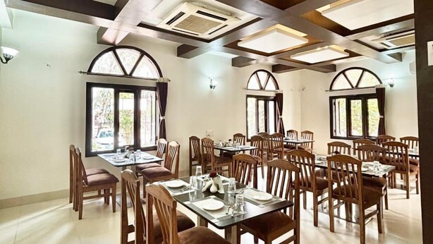 A spacious dining area with multiple tables and chairs, large windows, and a high ceiling with exposed beams and skylights. - Hotel Kailas Residency By Knight Hotel (Chhatrapati Sambhajinagar)