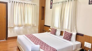 A hotel room with a large bed, a wooden headboard, a bedside table with a phone, and an air conditioning unit. - Hotel Kailas Residency By Knight Hotel (Chhatrapati Sambhajinagar)