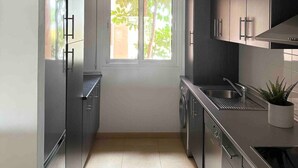A compact kitchen with dark cabinets, a built-in oven, and a window with a view of greenery. - Ground floor South facing apartment (Murcia)