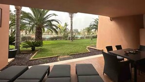 A patio area with a dining table and chairs, a small garden with palm trees, and a view of a pool. - Ground floor South facing apartment (Murcia)
