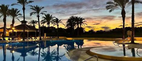 A swimming pool with palm trees and a building in the background during sunset.