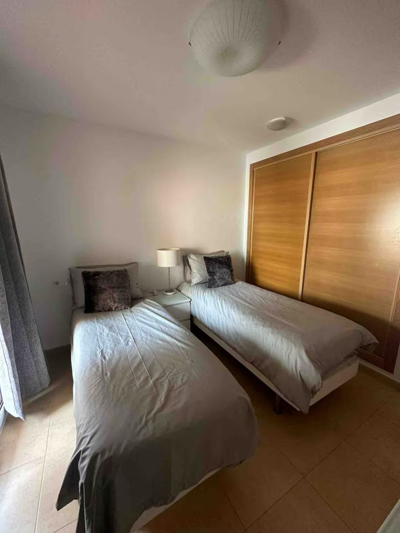 Un dormitorio con dos camas, un armario de madera, una mesita de noche con lámpara y una lámpara en el techo.