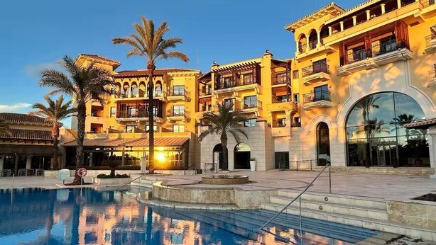 A hotel with a swimming pool, multiple balconies, and a courtyard with palm trees. - Ground floor South facing apartment (Murcia)