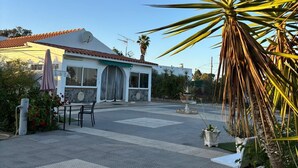 A building with a tiled roof, a covered patio area with tables and chairs, and a palm tree in the foreground. - Big and comfortable country house with garden in "Finca La Guindilla" with Pool (El Pico)