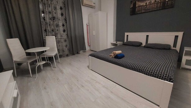 A modern bedroom with a bed, a chair, a small table, and a wardrobe. - Tudor Apartment Universitate (Bucharest)