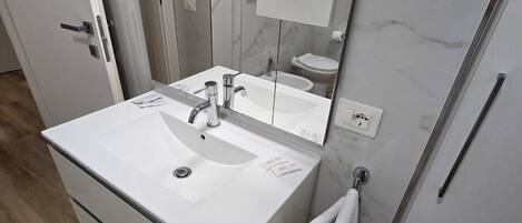 A modern bathroom with a white sink, mirror, and towel rack.