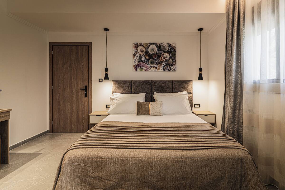 A hotel room with a large bed, a wooden door, a wall-mounted artwork, and two bedside lamps.