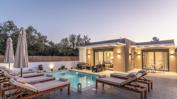 A modern outdoor pool area with lounge chairs, umbrellas, and a well-lit patio. - Lumior Villas Lux essence by 'elite' (Zakynthos)