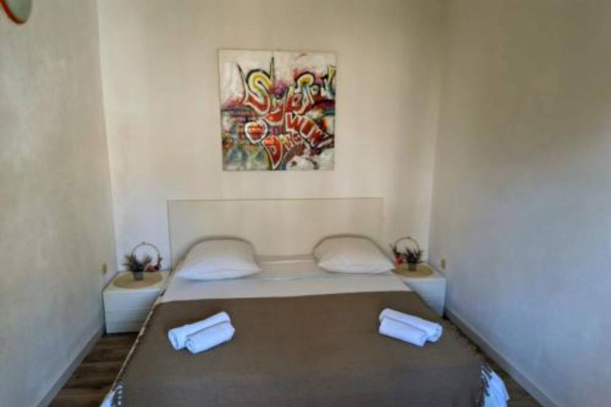 Quarto com cama, duas almofadas, cabeceira, mesa de cabeceira, quadro e toalha enrolada.