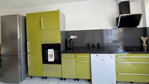 A modern kitchen with stainless steel appliances, a black countertop, and yellow cabinets. - Pretty T2 with garden (Pérols)