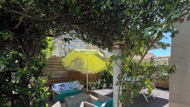 An outdoor patio with wicker furniture, a yellow umbrella, and a wooden fence. - Pretty T2 with garden (Pérols)