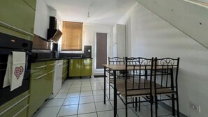 A kitchen with green cabinets, a dining table with chairs, and a window with blinds. - Pretty T2 with garden (Pérols)