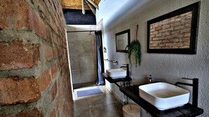 Un baño con pared de ladrillo, techo de madera, lavamanos blanco, espejo y planta colgante.