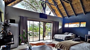Una habitación con techo de paja, cama, sofá, mesa de comedor y vistas al exterior.
