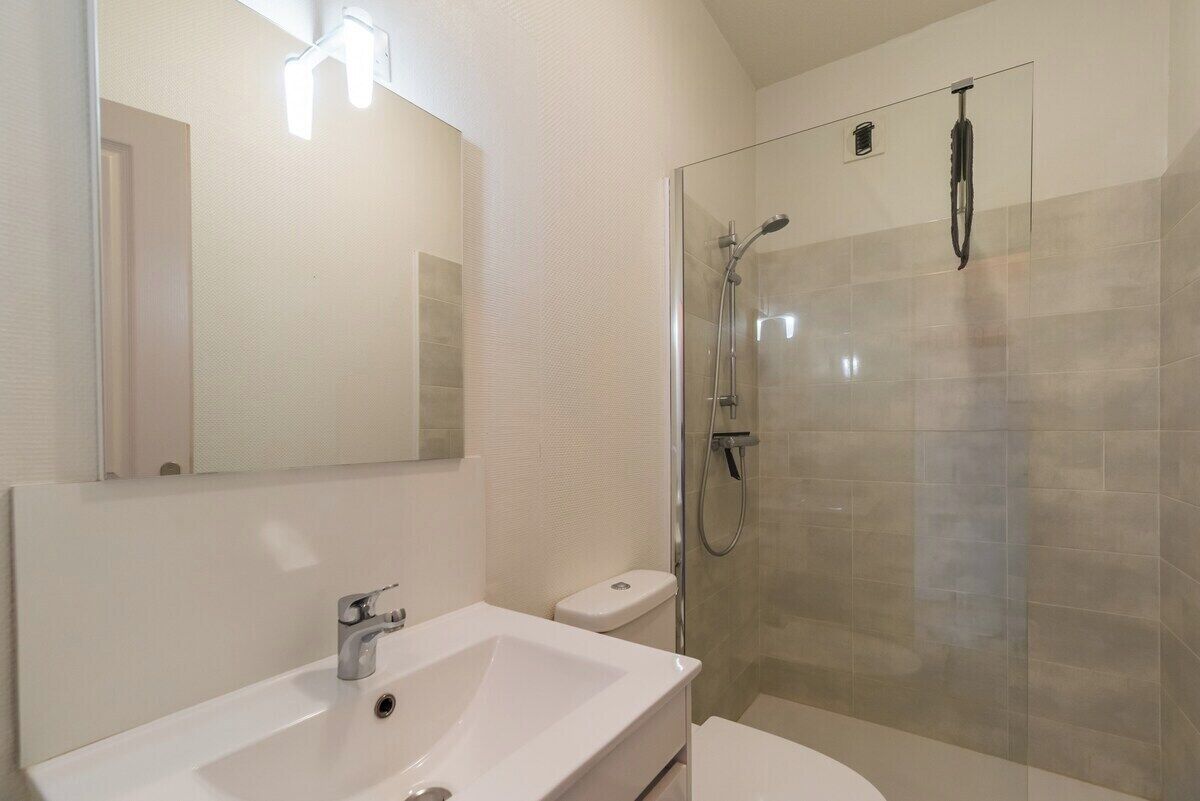 Ein Badezimmer mit weißem Waschbecken, Toilette, einer Duschkabine und einem Spiegel.