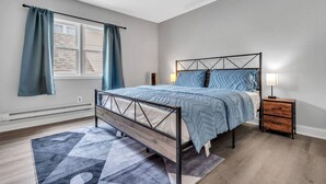 Une chambre à coucher avec un lit, une table de chevet, une fenêtre avec des rideaux et un tapis à motifs.