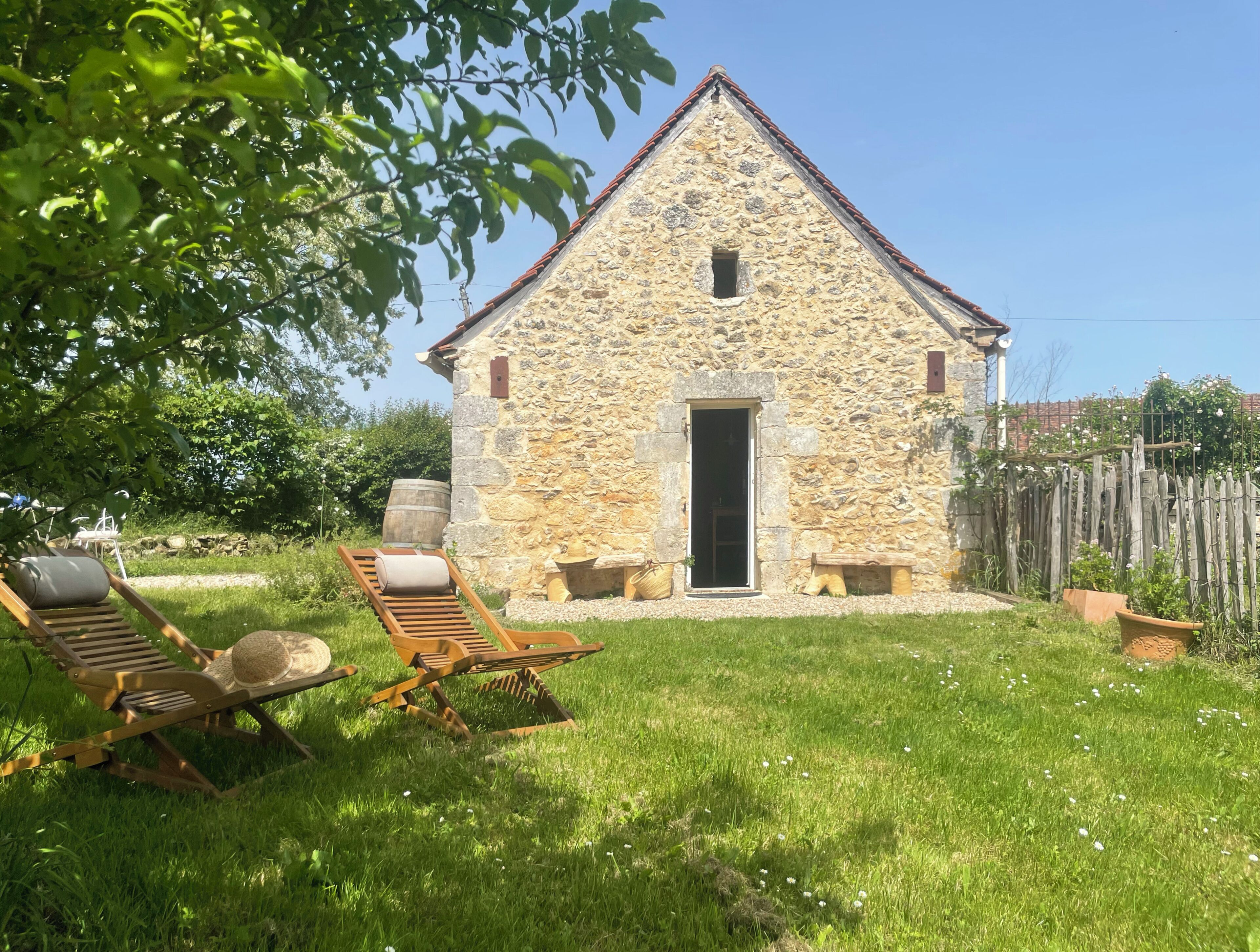 Un edificio in pietra con una porta e una finestra, circondato dall'erba e due sedie di legno.
