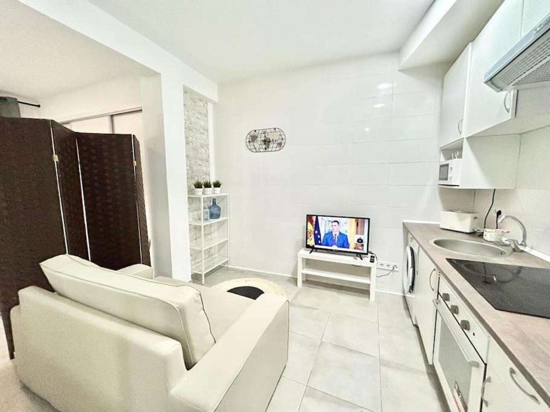 A modern kitchen with white cabinets, a built-in oven, and a small TV on a stand.
