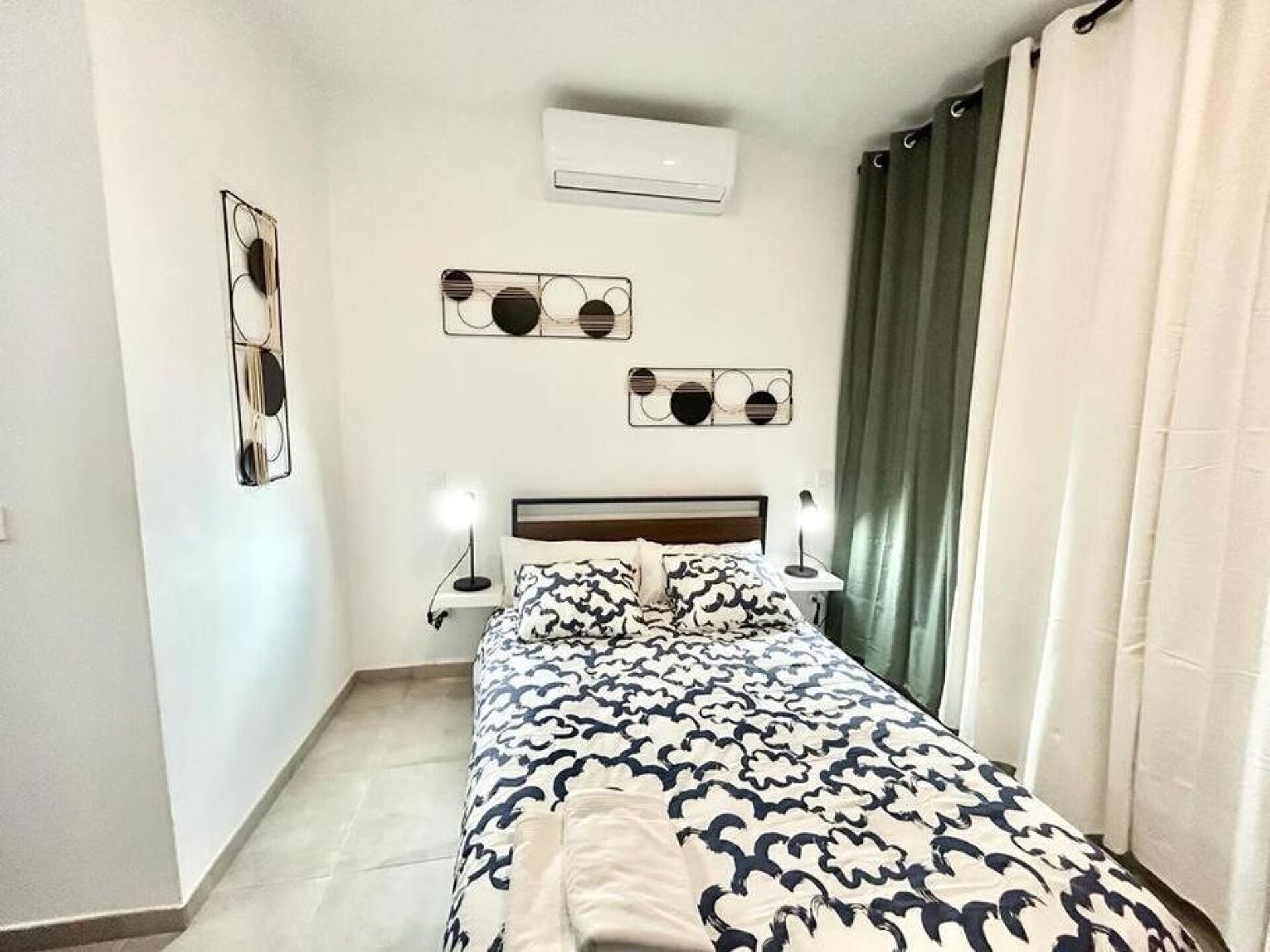Une chambre à coucher comprenant un lit, des lampes de chevet, un appareil de climatisation et des œuvres d’art murales.