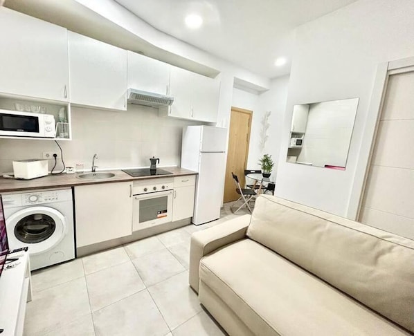 A compact kitchen with a washing machine, microwave, stove, and sink.