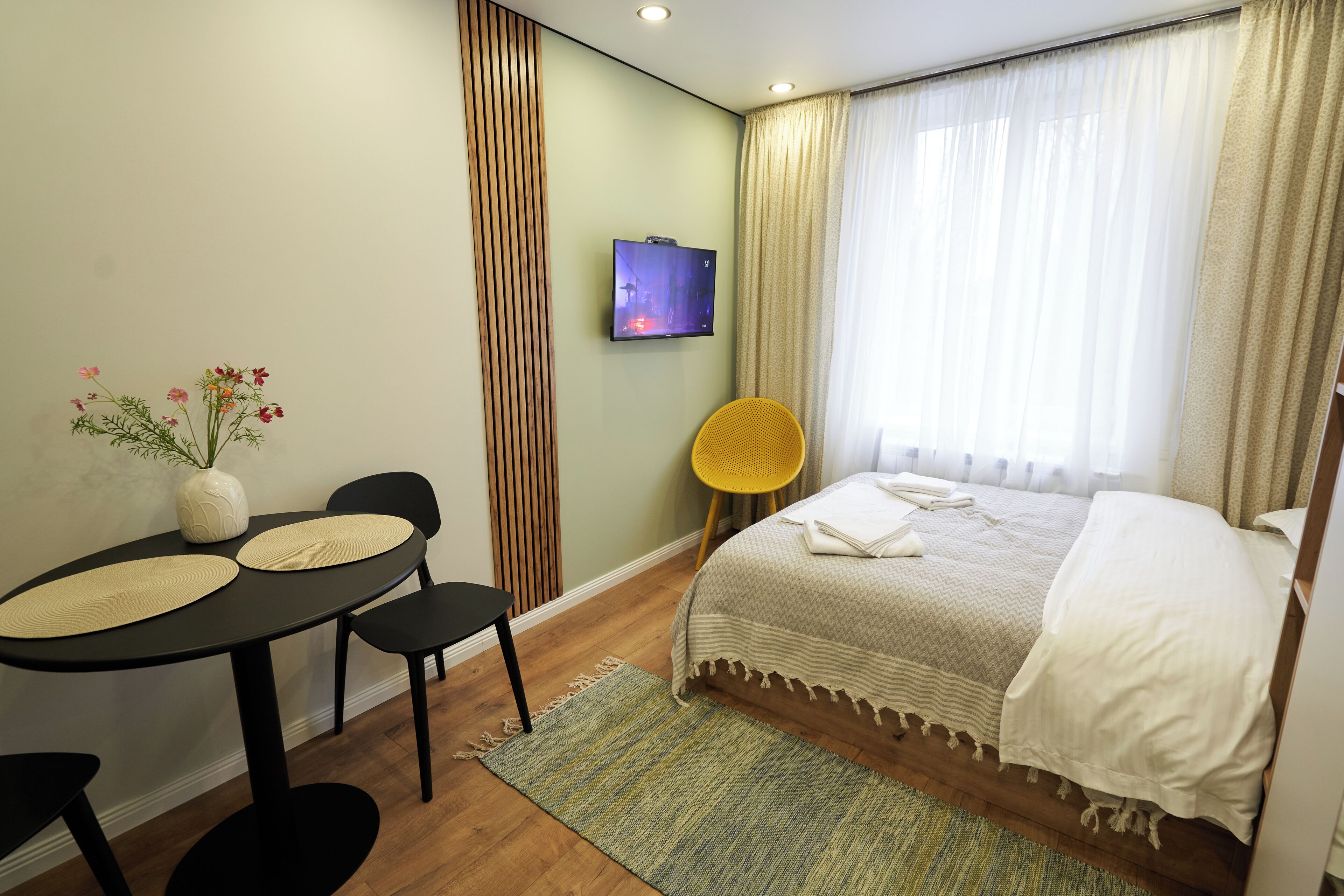 Une chambre d’hôtel avec un lit, une télévision, une table à manger avec des chaises et une petite plante.