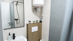 Moderni kylpyhuone, jossa on jalkapallipylväsmallinen pesuallas, wc ja lasinen suihkuseinä.