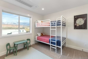 Um dormitório em estilo beliche com escrivaninha e cadeiras, uma janela com vista para montanhas e um quadro de um planeta.