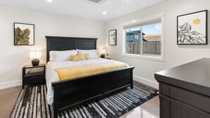 Une chambre à coucher avec un lit, des tables de chevet, une fenêtre et des œuvres d’art accrochées aux murs.