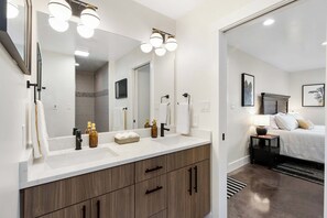 A modern bathroom with a large mirror, white countertop, and wooden cabinets.