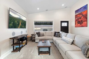 Una sala de estar moderna con un sofá modular, una mesa de centro, un televisor sobre un mueble, una ventana con vistas a un paisaje montañoso y una puerta con marco negro.