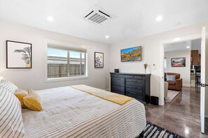 A bedroom with a bed, a window, a dresser, and a painting on the wall.