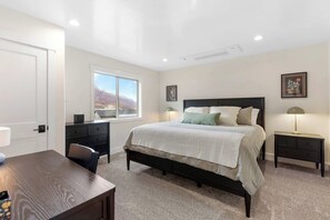 Un dormitorio con una cama grande, un escritorio, una silla, un ventanal con vistas y dos mesitas de noche con lámparas.