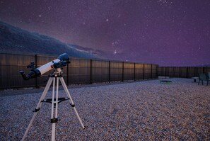 A telescope on a tripod in an outdoor area with a gravel ground, a fence, and a chair.