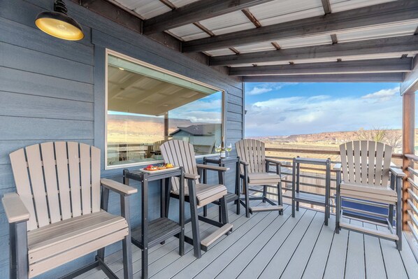 A covered outdoor seating area with Adirondack chairs and a table, overlooking a scenic landscape.