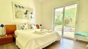 A bedroom with a bed, pillows, a nightstand, a lamp, a window, and a view of the outdoors.
