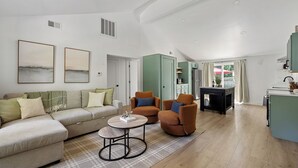 A modern living room with a sofa, two armchairs, a coffee table, and a kitchen area with cabinets and a refrigerator. - 2027 OPEN! (Unit B) Lakeside Home Close To Private Association Beach! (Lakeside)