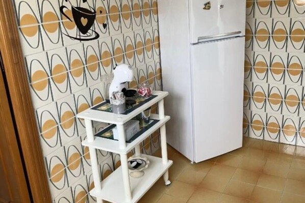 A kitchen with a white refrigerator, a white shelf with kitchen items, and a wall with a geometric pattern.