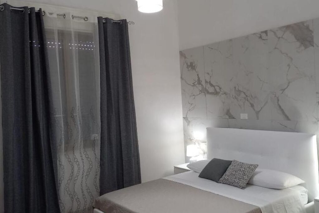 A bedroom with a bed, a nightstand, a lamp, and a marble-patterned headboard.