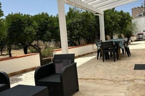 An outdoor patio area with stone flooring, a pergola, wicker furniture, and a table with chairs.