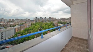 A balcony with a blue railing overlooking a cityscape with buildings and greenery.