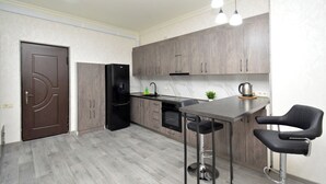 A modern kitchen with grey cabinets, a black refrigerator, a sink, and a bar area with two stools.