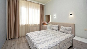 A bedroom with a bed, a nightstand, a dresser, a mirror, and a window with curtains.