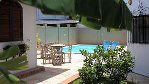 Un espace piscine agrémenté d’une table et de chaises, entouré d’un petit muret en briques et de plantes en pot.