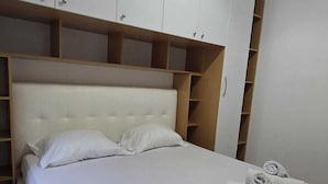 A neatly made bed with white linens and towels, a headboard, and a wardrobe with multiple compartments. - Tirent Apartment - Your Beach Home in Vlorë (Vlore)