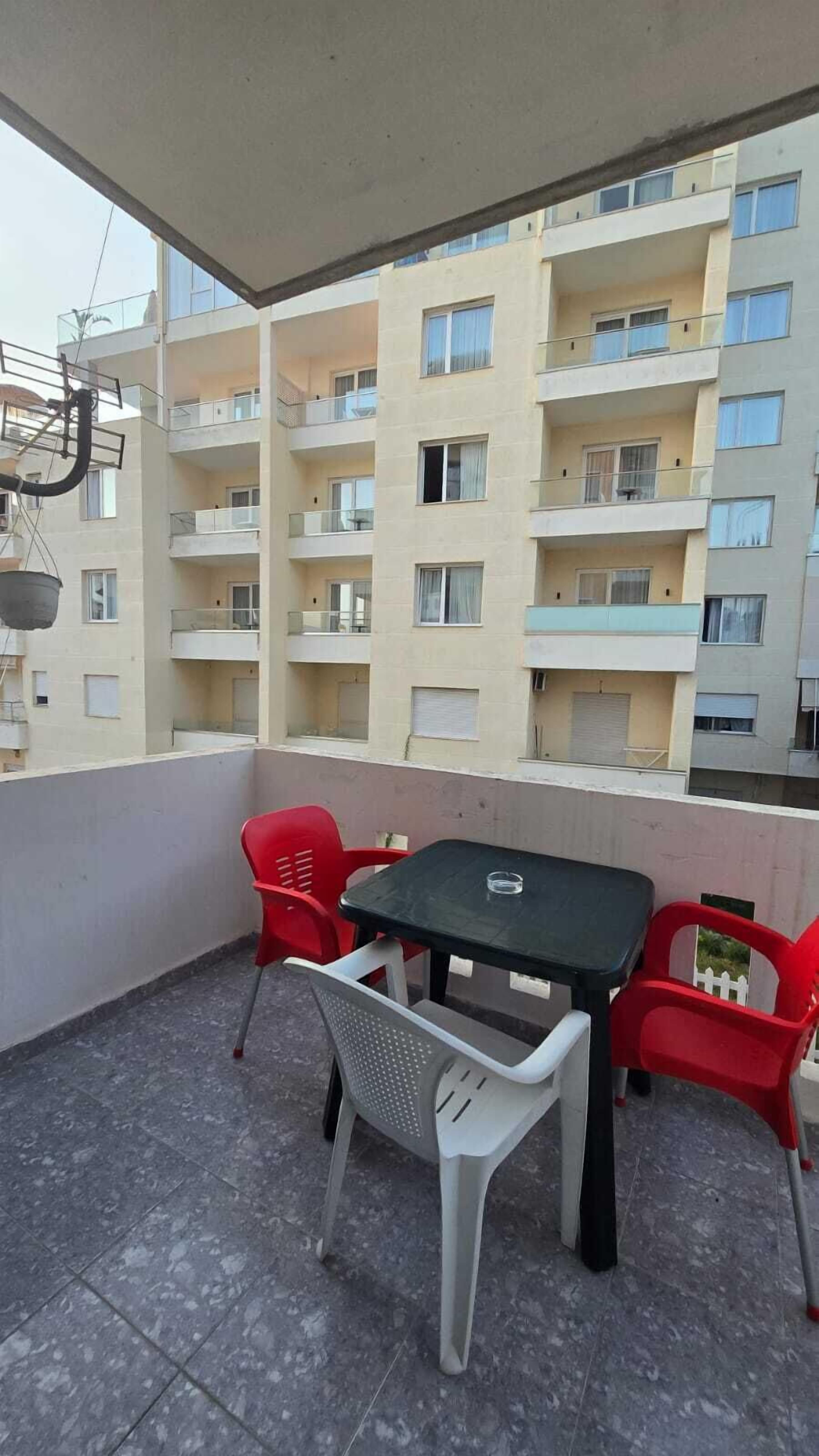 A balcony with a table and chairs, overlooking a multi-story building with balconies.