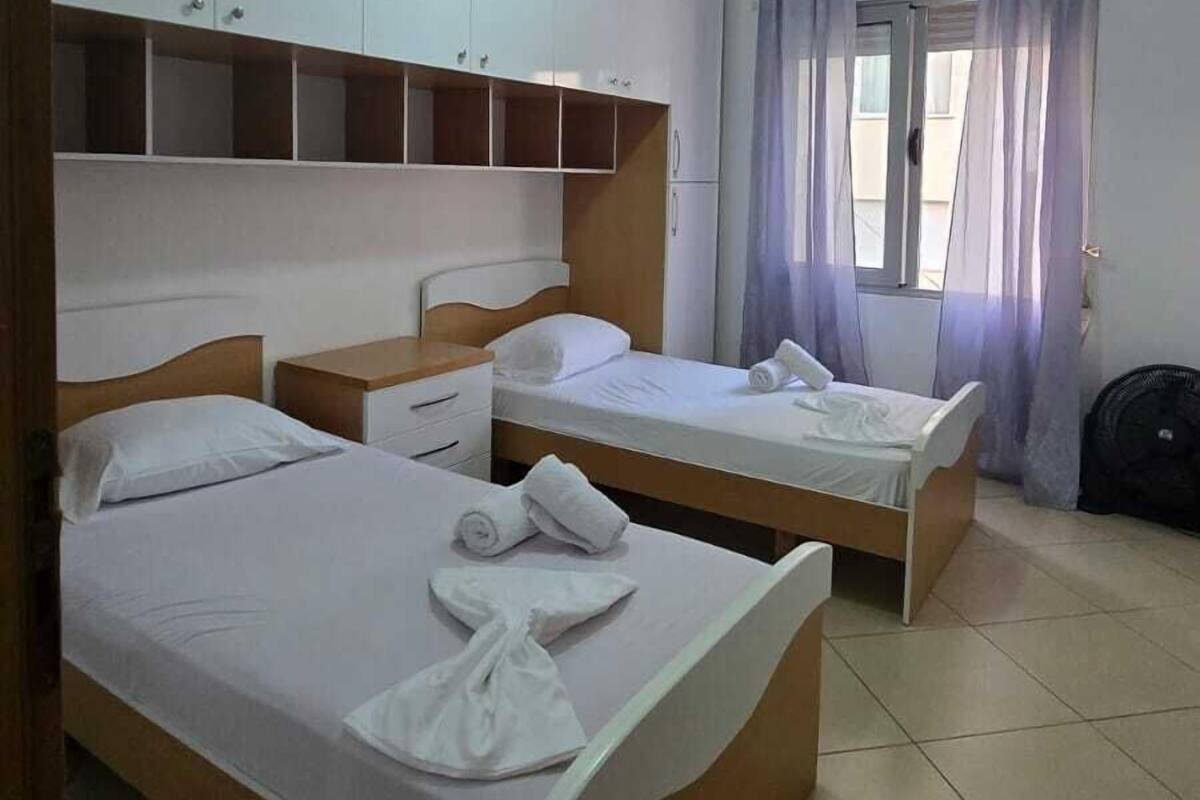 Ein Hotelzimmer mit zwei Einzelbetten, einem Kleiderschrank, einer Deckenleuchte und einem Fenster mit Vorhängen.